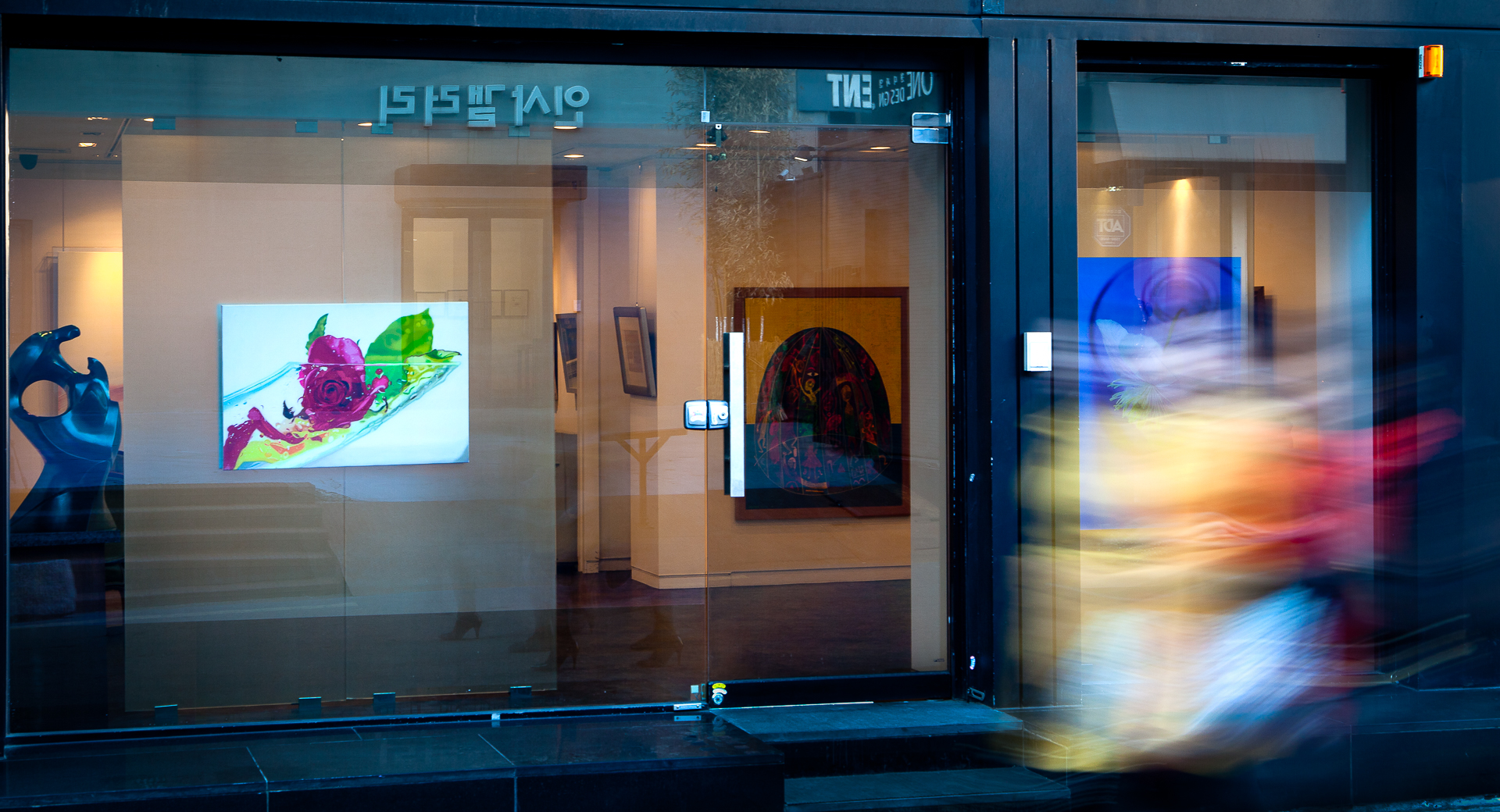 Long exposure photo of the window of an art galley in Seoul, South Korea with 3 women walking by.