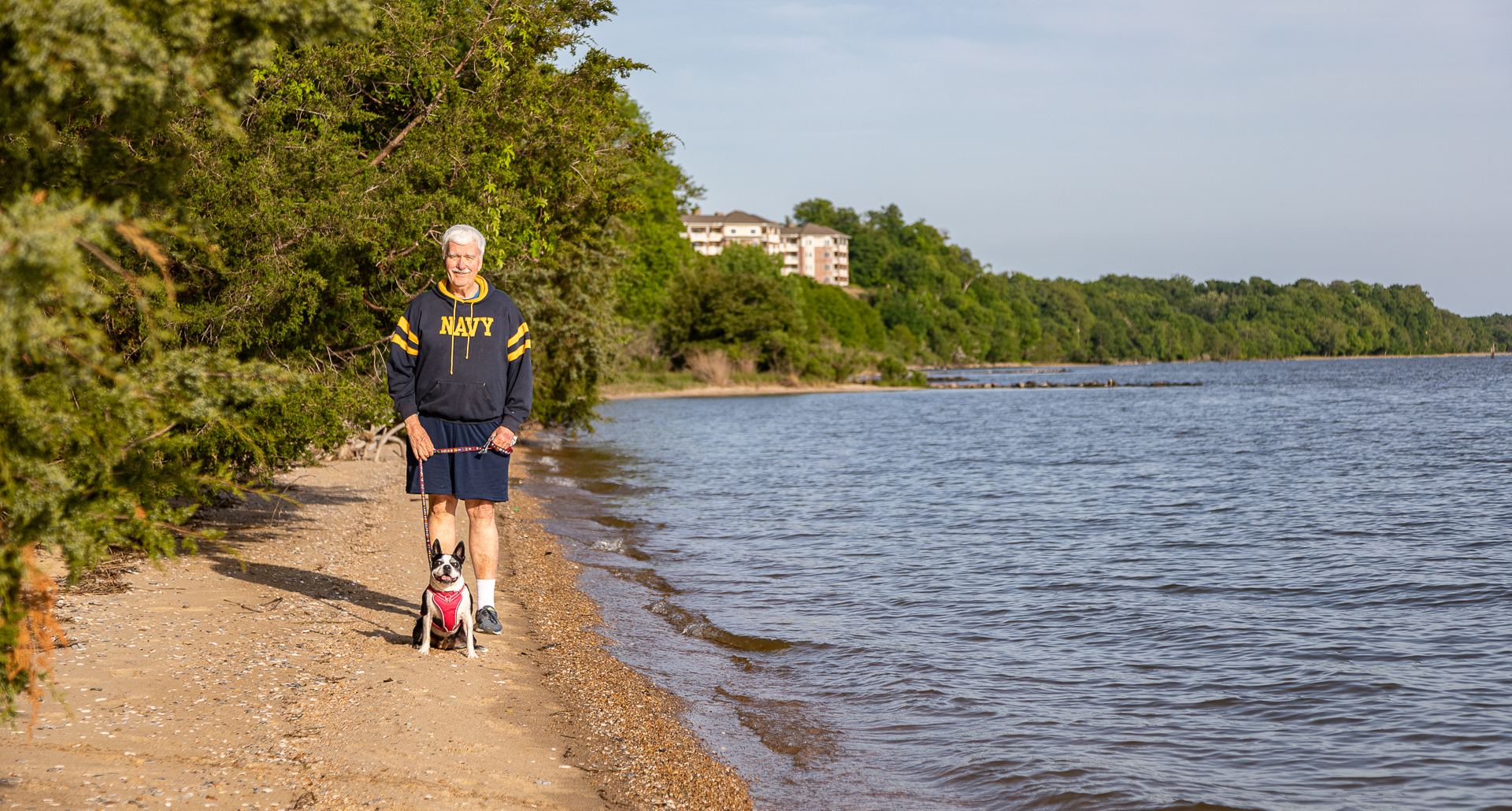 Man standing on narrow beach with his Boston Terrier.