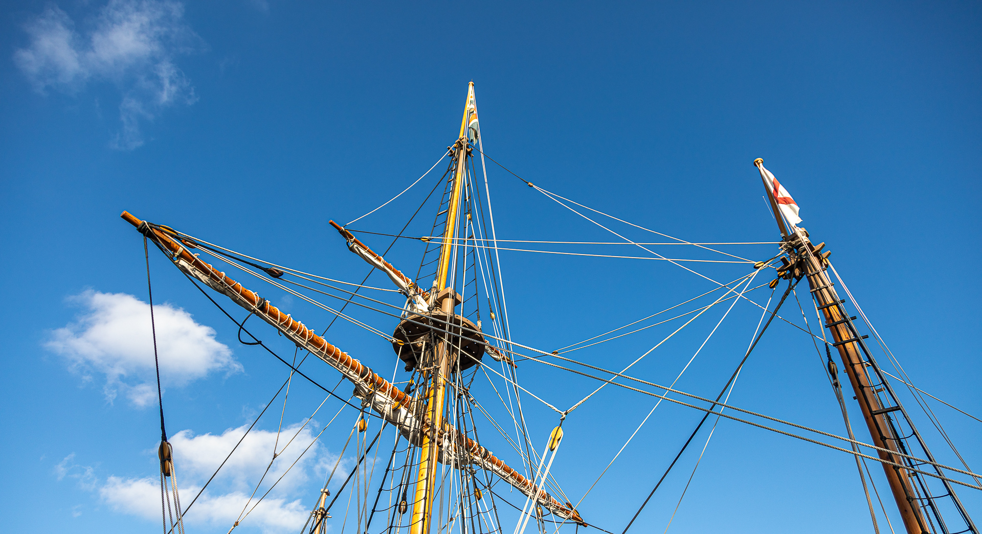 Photo of the rigging of a re-creation sailing ship in Jamestown Settlement, Virginia, against a blue sky with white fluffy clouds.