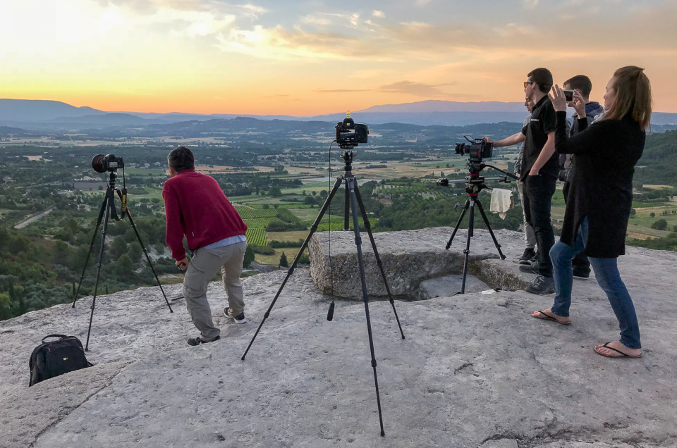 Photo of a group of photographers and videographers shooting the sunset at Gordes, France, using tripods.