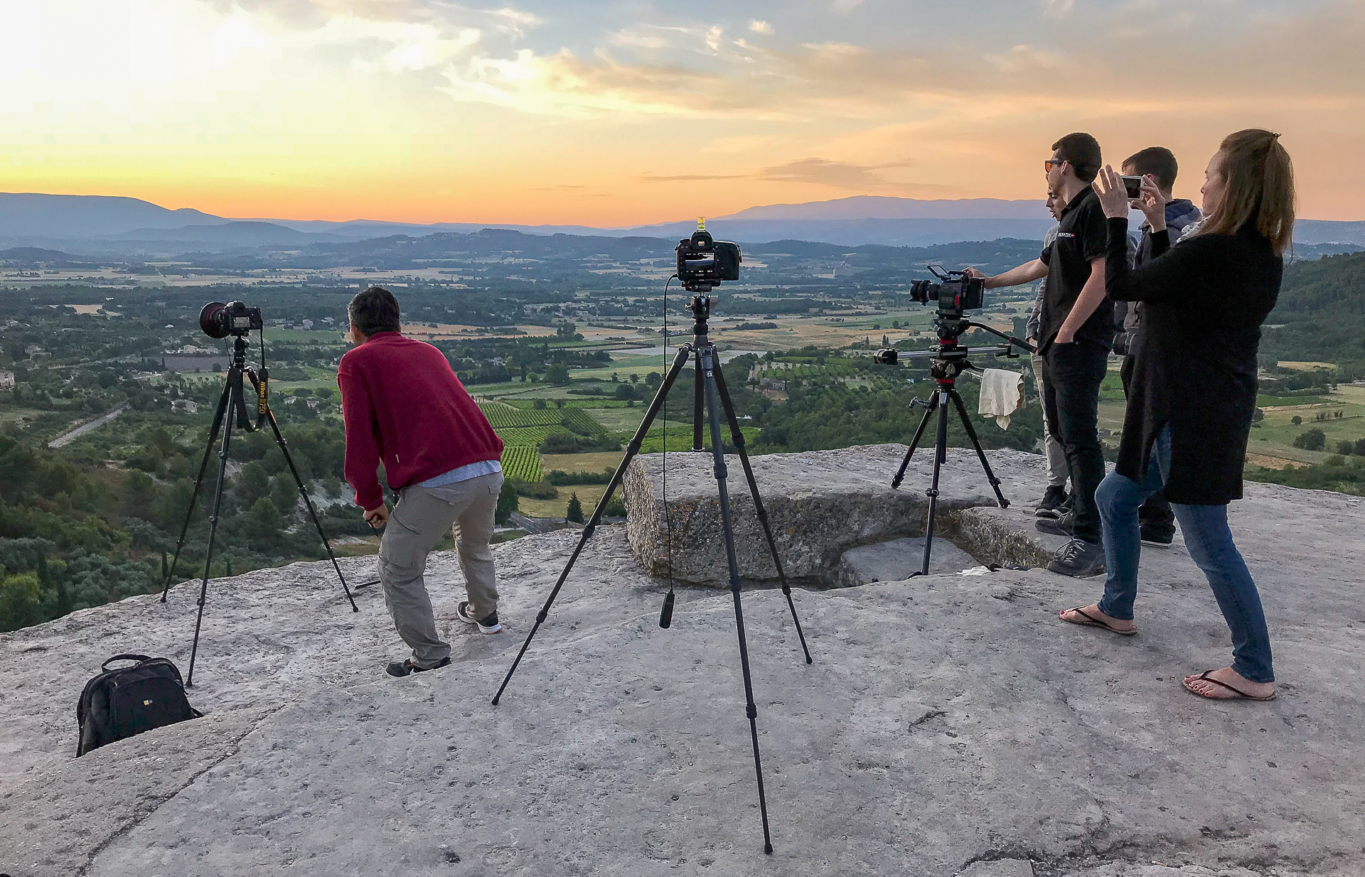 Photo of a group of photographers and videographers shooting the sunset at Gordes, France, using tripods.