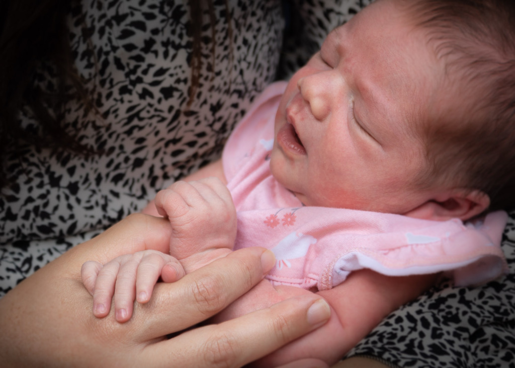 A new baby in her mother's arms. Her tiny fingers are holding onto her mother's hands.