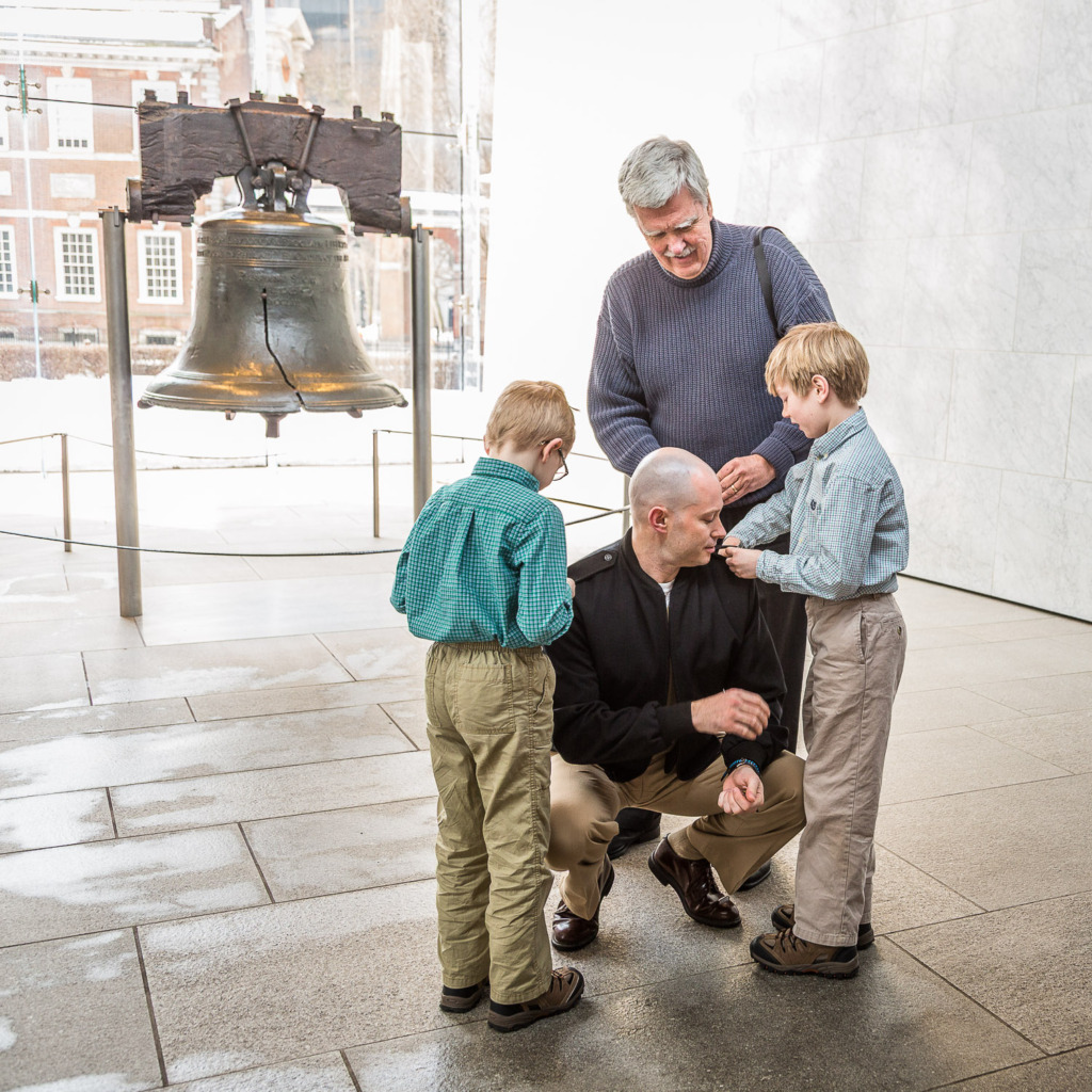 A family photo of a promotion ceremony in the Navy at the Liberty Bell in Philadelphia. The bright background is the reason why use manual mode.