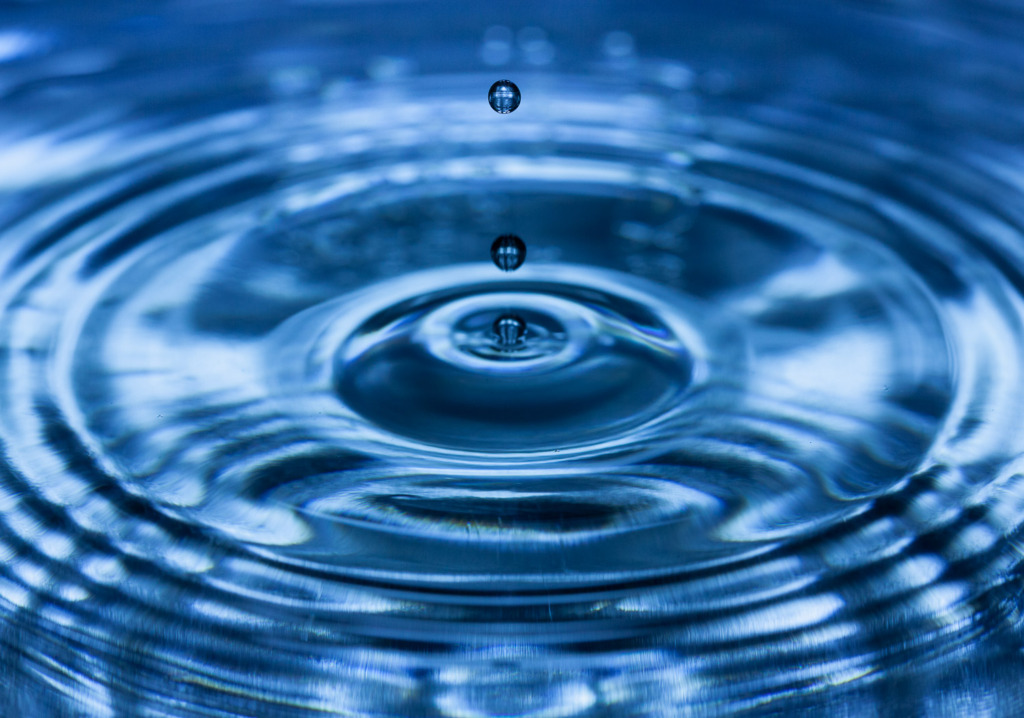 Three water drops frozen in the air as they fall into water. The water is blue and has concentric circles on it, caused by the dripping water.