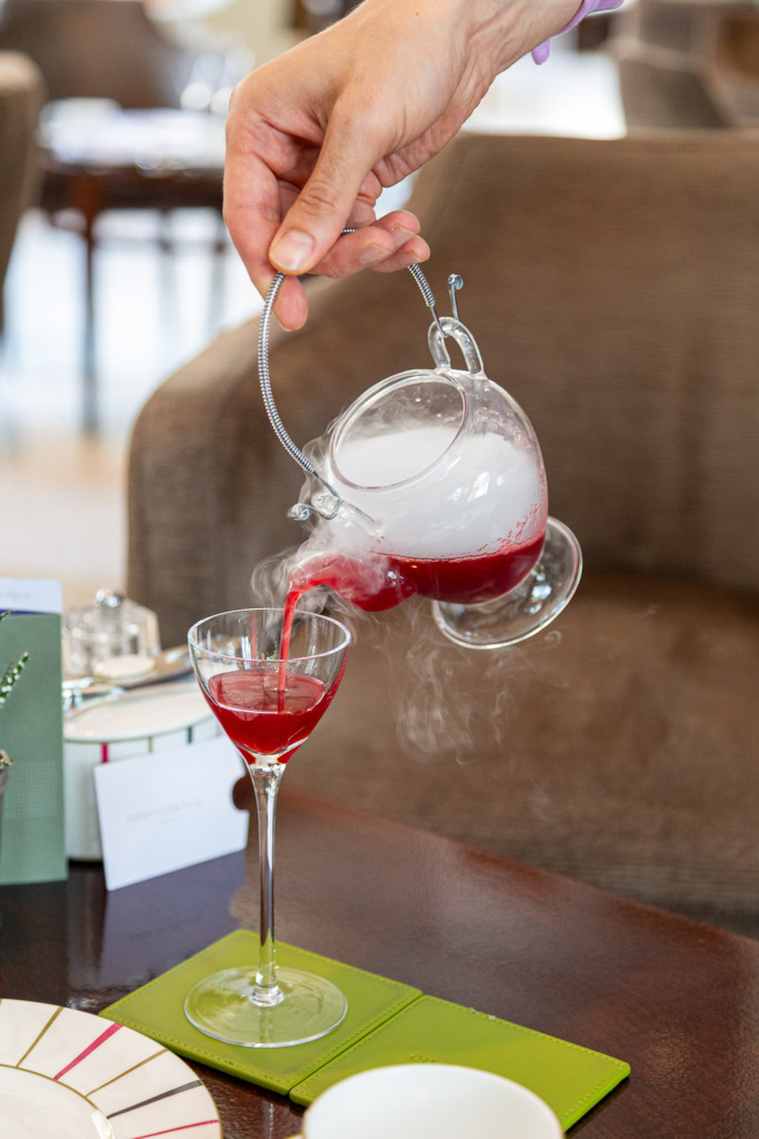 Smoky red drink being poured into a tall stem glass.