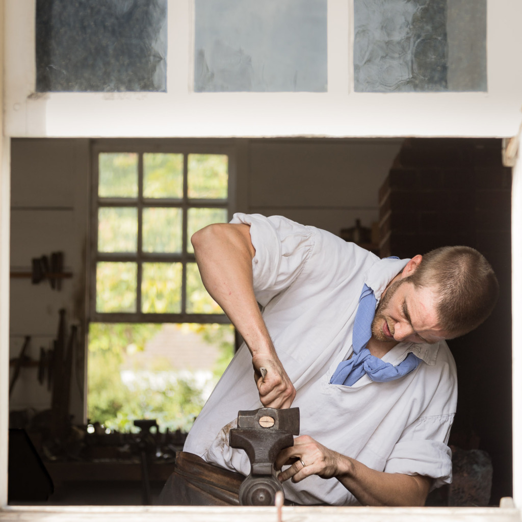 A blacksmith works to carve the wooden handle on a tool he has created in Colonial Williamsburg.