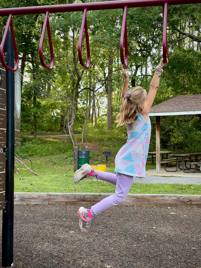 Image of a young girl hanging from bars on a playground.
