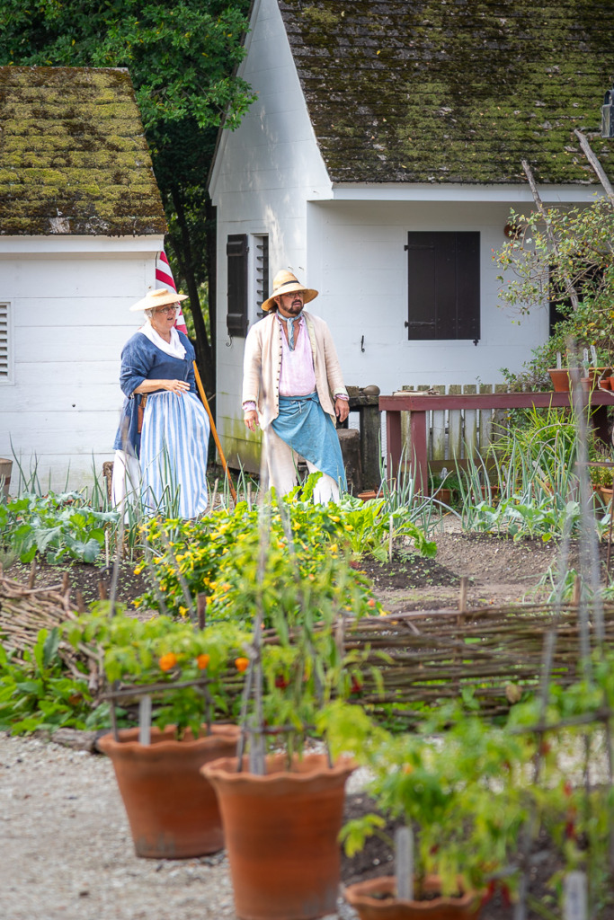 A photo of 2 interpreters in a garden in Colonial Williamsburg.
