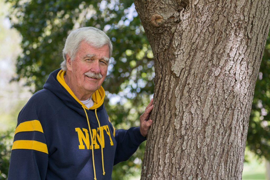 A man standing next to a tree while wearing a sweatshirt.