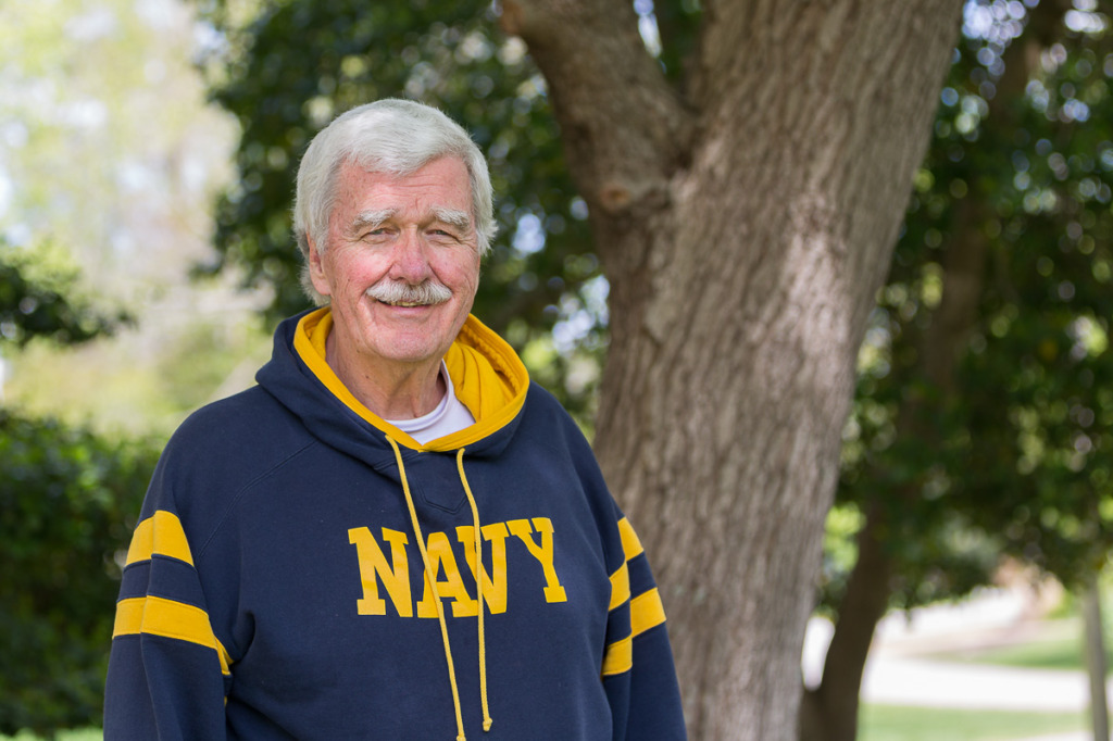 Study how to use aperture mode to understand how to create a shallow depth of field like in this photo of a man outdoors wearing a sweatshirt.